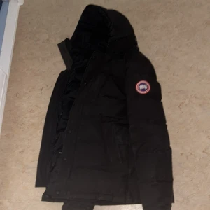 Canada goose parka 3805 style  - Säljer en svart dunjacka från Canada Goose med huva och dragkedja. Jackan har en klassisk design med långärmade ärmar och en logotyp på ärmen. Inga fel på den nypris 17 tusen