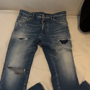 Dsquared2 jeans  - Snygga blå jeans från Dsquared2 med slitna detaljer och en cool, avslappnad look. De har en knappgylf och klassisk femficksdesign. Perfekta för en trendig stil. De är köpta på care of Carl och är i bra skick. 