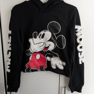 Svart hoodie med Musse Pigg från H&M - Säljer en svart hoodie från H&M med Musse Pigg-tryck på framsidan. Tröjan har långa ärmar med texten 'MICKEY MOUSE' längs ärmarna och en bekväm huva. Perfekt för Disney-fans! 🖤