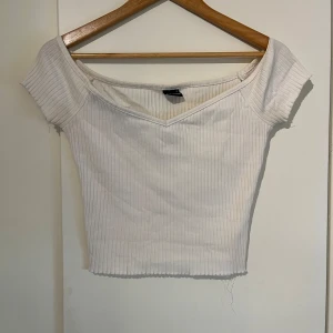Vit ribbad topp från Gina Tricot - Säljer en stilren vit ribbad topp från Gina Tricot. Toppen har en v-ringad design och korta ärmar, perfekt för en avslappnad look. Den är gjord i ett mjukt och stretchigt material som sitter bekvämt. Passar perfekt för dig som bär strl XS också!