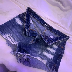 Blå jeansshorts med slitningar - Snygga blå jeansshorts med coola slitningar och fransiga kanter. Perfekta för en avslappnad stil. De har en klassisk femficksdesign och knäppning fram. (Shortsen är lite små i storlek så jag skulle beskriva dem som xs) De är för små för mig så det är därför jag säljer dem!💕💞