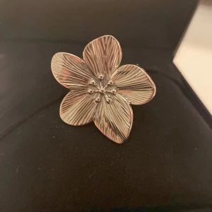 Silverfärgad blomring❤️ - Elegant silverfärgad ring formad som en blomma med detaljerade kronblad. Ringen har en justerbar design för att passa olika storlekar. Perfekt för att ge en stilfull touch till din outfit.