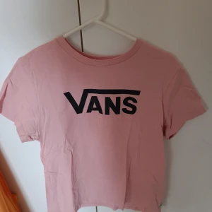Rosa t-shirt från Vans - Säljer en snygg rosa t-shirt från Vans med deras ikoniska logga i svart på framsidan. T-shirten är kortärmad och perfekt för en avslappnad stil. Passar bra till jeans eller shorts eller till vad som helst.