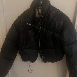 Svart pufferjacka från Bershka - Säljer en svart pufferjacka från Bershka. Jackan har en croppad design med dragkedja framtill. Perfekt för kyligare dagar och ger en trendig look. 🖤