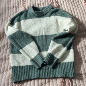 Randig stickad tröja i grönt och vitt från Lager 157 - Säljer en mysig stickad tröja med breda ränder i grönt och vitt. Tröjan har en normal passform och långa ärmar med ribbade muddar. Perfekt för kyliga dagar!