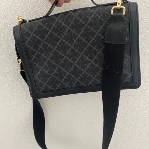 Väska från By Malene Birger med dustbag och delivery note - Svart och grå väska med mönster från By Malene Birger. Locket har magnetlås och axelremmen är justerbar med läderdetaljer. Väskan har guldfärgade metalldetaljer och två fack. Perfekt för att bära med stil. Finns delivery note samt dustbag.