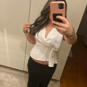 Vit omlottblus från Zara - Säljer en elegant vit omlottblus från Zara. Blusen har en v-ringad design med knytning i midjan för en smickrande passform. Perfekt för en stilren look. Passar som storlek S