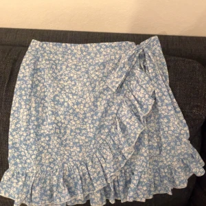 Blommig blå kjol från Shein - Söt blå kjol med vita blommor från Shein. Kjolen har volangdetaljer och en omlott-design som ger en romantisk touch. Perfekt för varma dagar och somriga tillfällen. 🦋