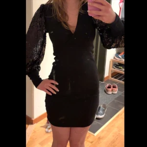 Svart klänning med paljettärmar - Snygg svart klänning med glittriga paljettärmar och v-ringning. Perfekt för en kväll ute eller fest. Den har en tight passform som framhäver figuren. Aldrig använd