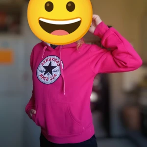Rosa hoodie från Converse - Säljer en snygg rosa hoodie från Converse med det klassiska Chuck Taylor All Star-märket på bröstet. Hoodien har en stor ficka framtill och justerbar huva med snören. Perfekt för en avslappnad stil.