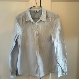 Ljusblårandig skjorta - Klassisk ljusblå skjorta med tunna vita ränder. Säljer därför att den är för liten. Skjortan är mycket sparsamt använd. 