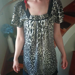 Leopardmönstrad kortklänning med svarta detaljer - Säljer en cool kortklänning med leopardmönster och svarta kantdetaljer. Klänningen har korta ärmar och en lös passform med rundad halsringning. Perfekt för dig som vill sticka ut med ett djurmönster!