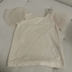 Vit topp med puffärmar från Zara - Säljer en söt vit topp från Zara med transparenta puffärmar i tyll. Toppen har rund halsringning och är tillverkad i mjuk bomull. Perfekt för dig som vill ha något stilrent men ändå unikt.