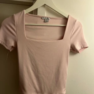 Ljusrosa topp med fyrkantig ringning från Amisu - Säljer en ljusrosa topp från Amisu(new yorker) med korta ärmar och snygg fyrkantig ringning. Toppen är i mjuk bomull och har en tight passform som framhäver figuren. Perfekt till jeans eller kjol!