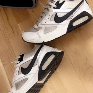 Nike Air Max vita och svarta sneakers - Säljer ett par klassiska Nike Air Max sneakers i vitt och svart. Skorna har en tydlig luftsula, svarta detaljer och den ikoniska swoosh-loggan på sidorna. Perfekta för dig som gillar sportig stil och bekväma skor.