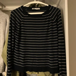 Svart och vit randig tröja från Zara - Säljer en svart långärmad tröja från Zara med tunna vita ränder. Tröjan har en klassisk rund halsringning och är i ett mjukt, stretchigt material. Perfekt för lager-på-lager eller som den är.