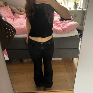 Svarta bootcut jeans - Säljer ett par svarta bootcut jeans med klassisk femficksdesign och knappgylf. Jeansen har en låg midja och lätt utsvängda ben. Perfekta för dig som gillar en tidlös och cool stil.