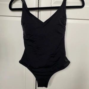 Svart baddräkt från H&M - En stilren svart baddräkt från H&M med v-ringad hals och justerbara axelband. Baddräkten har inbyggda kupor för extra stöd och en klassisk passform. Perfekt för stranden eller poolen!