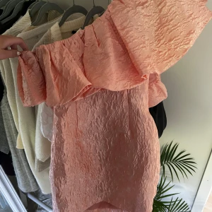 Ljusrosa offshoulder klänning från ASOS Luxe - Superfin ljusrosa klänning från ASOS Luxe med offshoulder-modell och volangdetalj upptill. Klänningen har en strukturerad, mönstrad yta och dragkedja i sidan. Perfekt för dig som letar klänningar till studentmottagninar eller bara generellt till sommaren! Säljer då den var för liten på mig, älskar den annars🥹💕💕