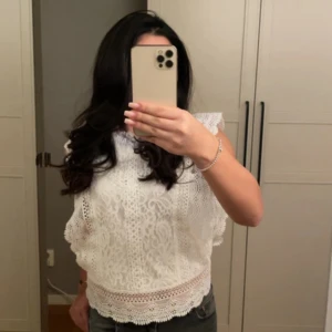 Vit spetsblus med volangkant från Only - Säljer en superfin vit blus i spets med vackra volangkanter längs ärmhålen och nederkanten. Blusen är ärmlös och har ett detaljerat blommigt mönster i spetsmaterial. Perfekt för dig som gillar romantisk och söt stil!