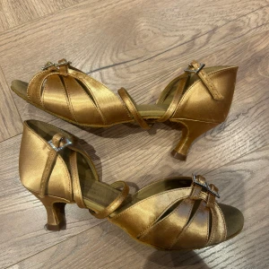 Golden open-toe dance shoes with bow - Selling a pair of elegant gold dance shoes with an open toe and a small heel. The shoes have nice bows at the front and narrow straps that cross the foot. Perfect for dancing or prom!