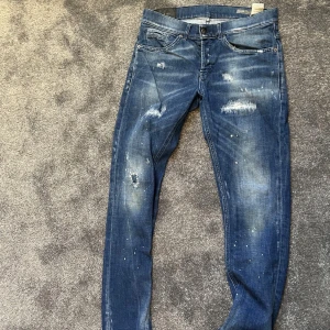 Blå Dondup  jeans med slitningar och färgstänk - Säljer ett par blå jeans från dondup med coola slitningar och färgstänk för en trendig look. Byxorna har klassisk femficksdesign, normal passform och knappgylf. Perfekta för dig som gillar en avslappnad och modern stil.