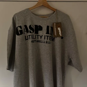 Grå ribbad tröja från GASP - Säljer en grå ribbad snygg tröja från GASP med svart och tryck både fram och bak. Tröjan har stor passform och är tillverkad i ett mjukt material. Perfekt för dig som gillar sportig och avslappnad stil.