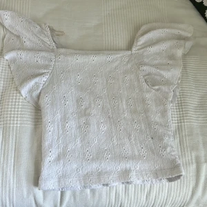 Gullig sommar top😍 - Söt vit topp från Kappahl med broderat hålmönster och stora volangärmar. Toppen har en rak passform och är tillverkad i ett lätt bomullstyg, perfekt för varma dagar.