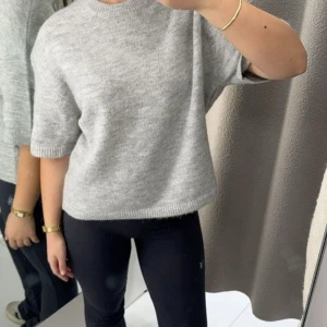 Ljusgrå stickad tröja - Säljer en ljusgrå stickad tröja med korta ärmar och rund halsringning. Tröjan har en avslappnad passform och är perfekt för lager-på-lager. Supermjuk och enkel att matcha till olika outfits.