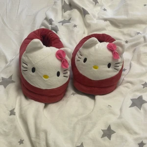 Hello Kitty tofflor i rött och vitt - Supergulliga Hello Kitty tofflor i rött och vitt med mjukt plyschmaterial. Tofflorna har ett stort Hello Kitty-ansikte framtill med rosa rosett och broderade detaljer. Perfekta för att mysa runt hemma. Passar mig bra som har 37 men skulle även passa 36/38