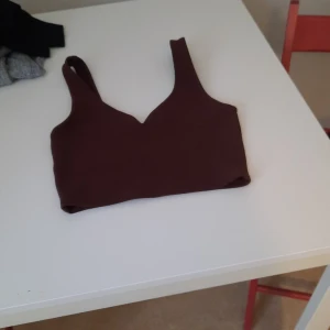 Brun croppad linnetopp - Säljer en brun croppad linnetopp med breda axelband och djup v-ringning. Perfekt för varma dagar eller som ett lager under en skjorta. Enkel och stilren design.