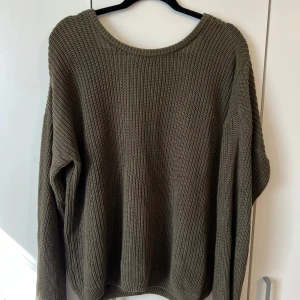 Olivgrön stickad tröja med v-ringning - Säljer en olivgrön stickad tröja med djup v-ringning i ryggen. Tröjan har lång ärm och är oversized i modellen.