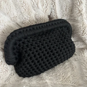 Svart handvirkad clutch / väska - Säljer en svart handvirkad clutch / handväska som jag har virkat! Väskan är i ett mjukt garn och är väldigt rymlig! Kan bäras i handen som en clutch eller bäras i handtaget. 