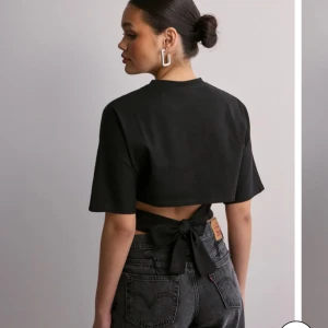 Svart t-shirt med rosett i ryggen från Nelly - Säljer en svart t-shirt från Nelly knytband som man kan knyta till en rosett i ryggen, som ger en snygg detalj baktill. Man kan både använda T-shirten på en vardag men också om man vill vara finklädd. Använd ca 5 gånger, den är som ny. Säljer pågrund av att den inte kommer till användning längre. Pris kan diskuteras.