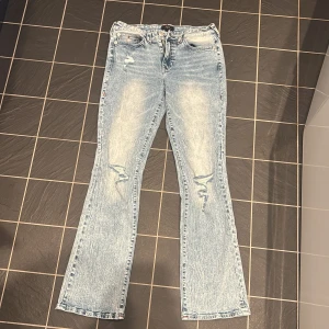 True Religion Becca Mid Rise Bootcut Jeans - Säljer ett par ljusblå jeans från True Religion, modell Becca Mid Rise Bootcut. Jeansen har bootcut-passform, klassiska fem fickor och snygga slitningar framtill. Perfekta för dig som gillar en avslappnad men trendig stil.