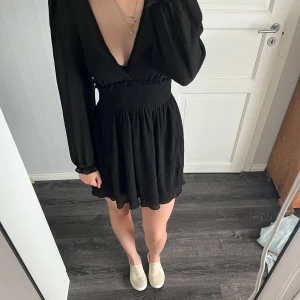 Svart långärmad klänning med djup v-ringning - Svart kortklänning med lång ärm och djup v-rigning. Klänning är från NAKD använd typ 1 gång så jätte bra skick! 🤗