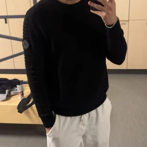 Svart stickad tröja från Canada Goose - Säljer en svart stickad tröja från Canada Goose med rund halsringning och diskret logotyp på ärmen. Tröjan är enkel och stilren, perfekt för dig som gillar klassisk design. Tillverkad i Italien, väldigt hög kvalité och väldigt skön, för en skön sommar look rekommenderar starkt! För mer frågor / bilder hör gärna av er! 🙏 passar både S/M (har själv S och passar mig perfekt) 