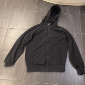 Svart hoodie med dragkedja Peak performance  - Säljer en svart hoodie med dragkedja och huva ifrån Peak performance . Tröjan har långa ärmar, två fickor framtill och ribbade muddar vid ärmslut och nederkant. Perfekt för en avslappnad stil.
