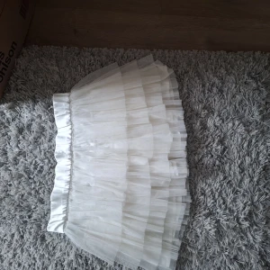 Vit tyllkjol med volanger - Säljer en fluffig vit kjol i tyll med flera lager volanger. Kjolen har resår i midjan och är perfekt för dig som vill ha en söt och luftig look. Passar till många olika stilar och är superenkel att matcha.