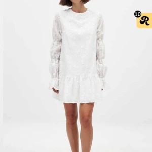 Vit blommig kortklänning med volang och öppen rygg - Superfin vit kortklänning med blommigt mönster, volang nertill och långa puffärmar. Klänningen har öppen rygg med knytband upptill och är perfekt för sommarens tillfällen.