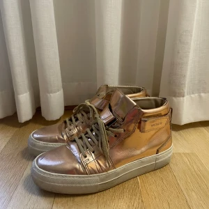 Metallic rosa sneakers från Axel Arigato - Säljer ett par snygga metallic roséguld sneakers från Axel Arigato. Skorna har hög kant, snörning och vit platt sula. Ganska så använda men inga större slitage än vad som visas på bilder! 🩷