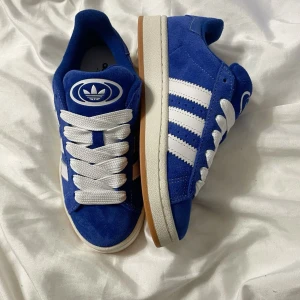 Blå Adidas Campus sneakers i mocka - Säljer ett par blå Adidas Campus sneakers i mocka med vita ränder och vit sula. skorna är använda max tre gånger och man får med både vita och blåa snören. Storlek 39 1/3! Nypris: 1599. Pris kan diskuteras.❤️❤️