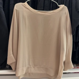 Beige blus med trekvartsärm - Säljer en stilren beige blus med rund halsringning och trekvartsärmar. Blusen har en lös passform och är tillverkad i ett mjukt, lätt material som ger ett snyggt fall. Perfekt att matcha med både jeans och kjol.