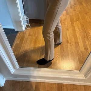 Beiga kostymbyxor med bootcut - Snygga beiga kostymbyxor med bootcut och hög midja. Byxorna har pressveck, hällor för bälte och stängs med dragkedja och knapp. Perfekta för en stilren look och passar till många olika outfits. Midjemått: 76 cm Innerbenslängd: 70 cm! Jag är 1,58 m lång och de är bra i längden på mig! 💕Pris går att diskutera! 💕