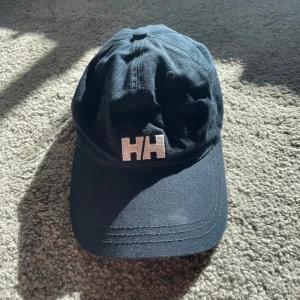 Mörkblå keps från Helly Hansen - Helly Hansen keps som passar perfekt för dig som äger en båt eller har allmänt bra stil. Den är använd 1-2 gånger och så gott som ny. Köptes för 400 kronor.