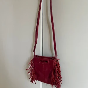Vinröd Maje väska - Säljer en vinröd axelväska från Maje. Väskan har en justerbar axelrem och är tillverkad i skinn. 
