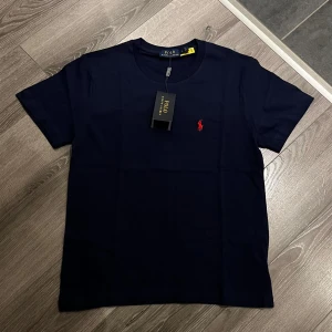 Blå Polo Ralph Lauren T-shirt  - Säljer en helt ny mörk blå Polo Ralph Lauren T-shirt med hög kvalite för väldigt bra pris. Den är helt ny med prislapp och oanvänd. Perfekt för sommaren!Det står L på tröjan som storlek men passar som S/M. Skriv vid intresse!!!!