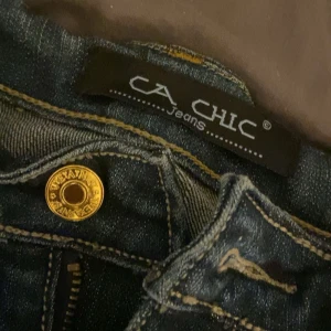 Mörkblå jeansbyxor från CA Chic - Säljer ett par mörkblå jeansbyxor från CA Chic med snygga guldfärgade knappar och dragkedja. Bakfickan har ett broderat mönster i gult som ger en unik touch. Klassisk femficksmodell med kontrastsömmar. Har ärvt dessa av min mamma och aldrig använt då dem inte passar mig. Skulle säga stl 38/39/40 (S,M)