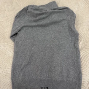 Grå halvzip tröja i ullblandning - Säljer en stilren grå tröja med halv dragkedja i kragen. Tröjan har lång ärm och ribbade muddar vid ärmslut och nederkant. Perfekt för lager-på-lager och enkel att matcha med det mesta.