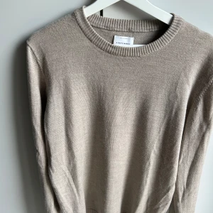 Beige merinoulltröja från A Day's March - Säljer en stilren beige tröja i mjuk merinoull från A Day's March. Tröjan har rund halsringning och långa ärmar, perfekt för lager-på-lager under kyliga dagar. Enkel och klassisk design som passar till det mesta. Bara att fråga på om det skulle vara något eller behöva mer bilder!